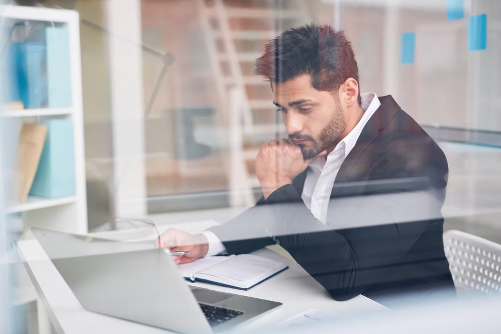 Homme en costume assis sur une chaise qui travaille sur un ordinateur installé sur son bureau